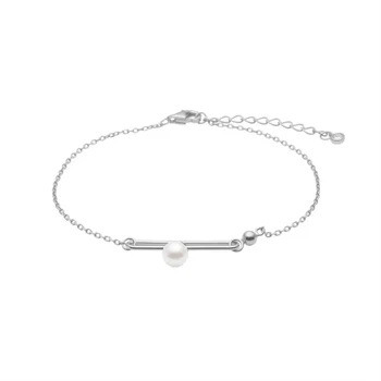 Armbånd med central perle på guld barrelement, delikat kæde, bæres af kvinde i hvid skjorte.