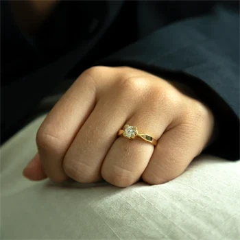 Hånd med gylden ring, rund sten i midten. Enkel og glat stil.