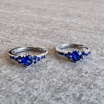 Sølvcreoler med stor blå zirkonia i midten og små blå sten langs ringen på en grå baggrund.